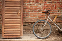 A wooden door and a bicycle lean against a brick wall.