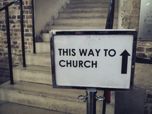 A sign next to some stairs showing 'this way to church' 
