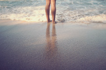 legs standing in the ocean on a beach 