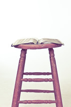 Open Bible op top of wooden stool.