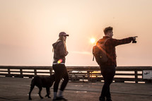 couple and their dog walking on a pier at sunset 