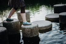 A woman balances as she steps out on a stone path through a lake.