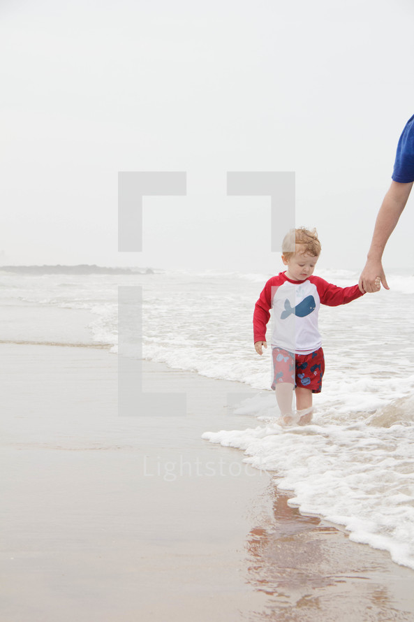 father and son walking in water on a beach 