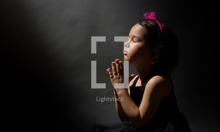 Little girl praying, isolated black background