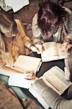young women holding hands in prayer over Bibles at a Bible study