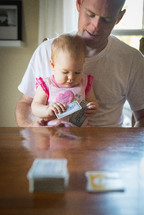 A baby girl with playing cards sitting in her father's lap.