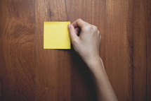 an arm placing a blank sticky note on a wood desk 