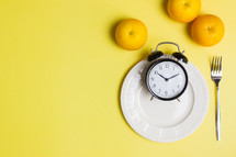 Diet concept with oranges, clock and fork over the yellow background. 