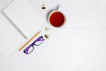 open notebook, tea cup, reading glasses on a desk 