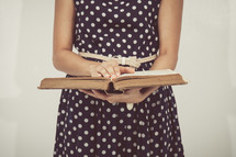 torso of a woman in a polka dot dress reading a Bible 