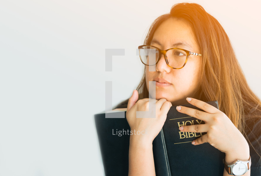 a young woman holding a Bible and thinking 