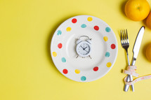 Diet concept with oranges, clock and fork over the yellow background. 