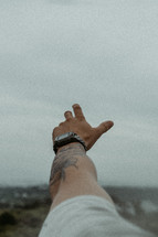 Man's arm with tattoo reaching toward sky