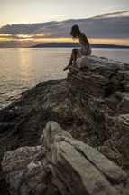 a woman sitting on a rock over looking the ocean 
