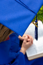 female graduate praying over a Bible 