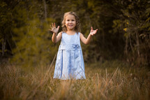 toddler girl standing outdoors with raised hands 