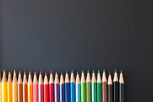 row of rainbow colored pencils on a black background 