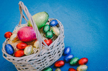 Colored easter eggs in a wicker basket on a blue background