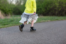 a girl child in boots and skirt stomping down a paved path 