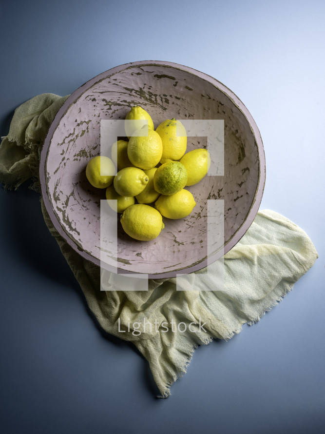 Pink bowl of lemons with fabric on blue background