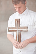 man holding a wooden cross with his head bowed in prayer