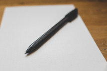 A pen sits on a sheet of blank paper on a desk