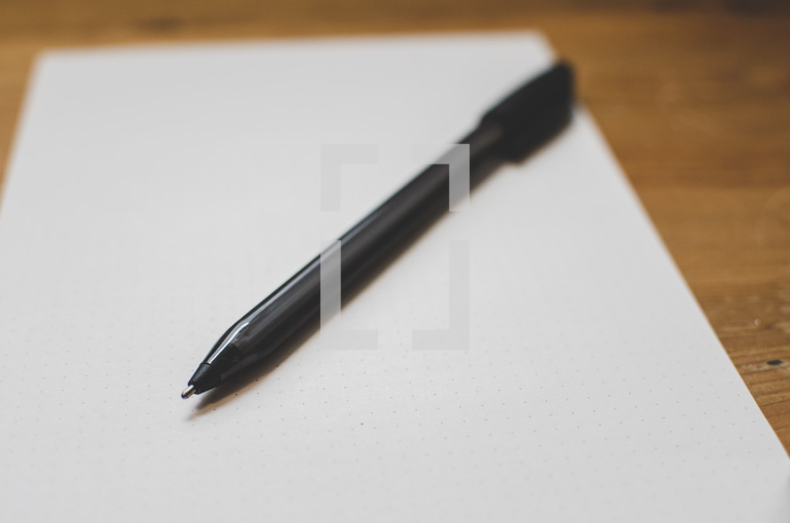 A pen sits on a sheet of blank paper on a desk