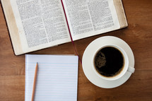 open Bible, notepad, pencil, and coffee cup on a table 