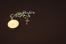 Rosary and single candle laying on a black background