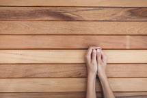 praying hands over a wood table 