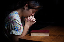a woman in prayer over a Bible 