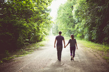 a couple walking holding hands on a dirt road 