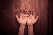 cupped hands holding pills and a needle 