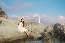 a woman sitting on rocks along a shore 