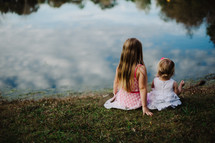sisters sitting by the edge of a pond