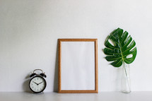alarm clock, blank frame, and vase with tropical leaf 