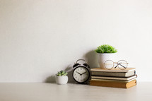 Reading concept with books, green leaves and clock on wooden table. 