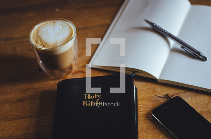 A coffee, phone, notebook, pen and bible on a table