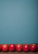 A line of red apples on a wooden surface against a blue background.