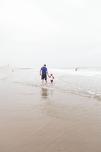 father and son walking in the water on a beach 