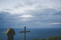 woman standing near a cross by the ocean 