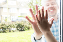Boy holding his hand against a window mirroring his fathers hand