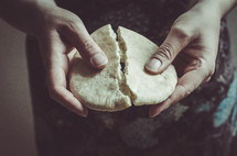 A woman breaking a piece of bread.