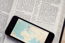 A phone with a world map showing Europe, Africa & Asia sitting on a bible open to the great commission