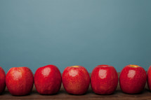 row of red apples on a desk 
