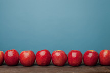A line of red apples on a wooden surface with a blue background.