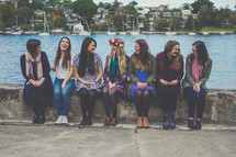 group of female friends sitting on a wall near a river 