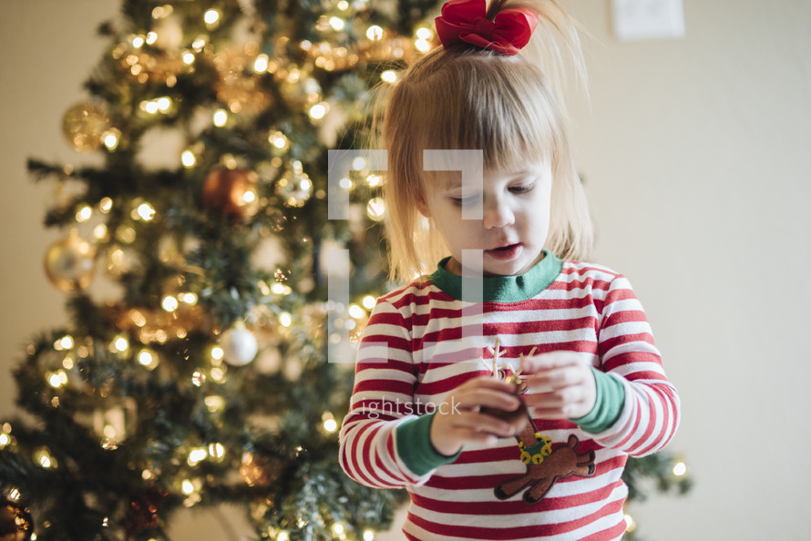 a toddler girl standing in front of a Christmas tree