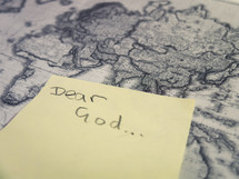 A yellow post-it sticky note with the handwritten words 'dear God' stuck to an antique style world map.