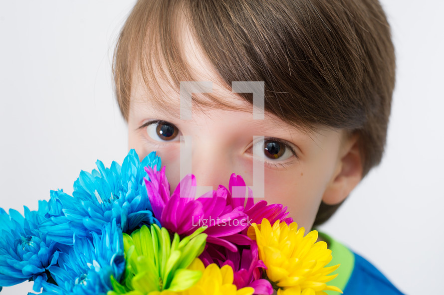 Boy holding a bouquet of flowers in front of his face.